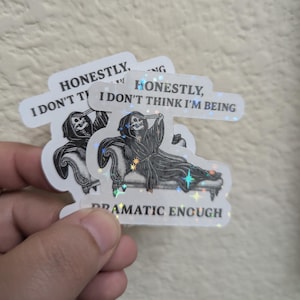 May include: A stack of stickers with a holographic finish. Each sticker features a black and white illustration of the Grim Reaper reclining on a chaise lounge. Text on the stickers reads "HONESTLY, I DON'T THINK I'M BEING DRAMATIC ENOUGH."