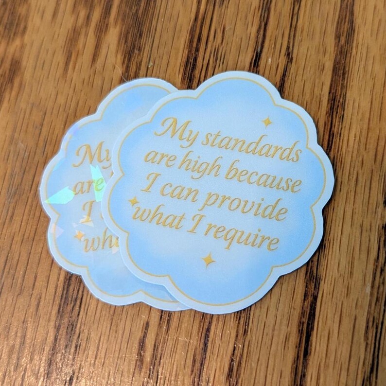 May include: Two cloud-shaped stickers with a light blue background and gold text. The text reads "My standards are high because I can provide what I require." The stickers have a holographic sheen.