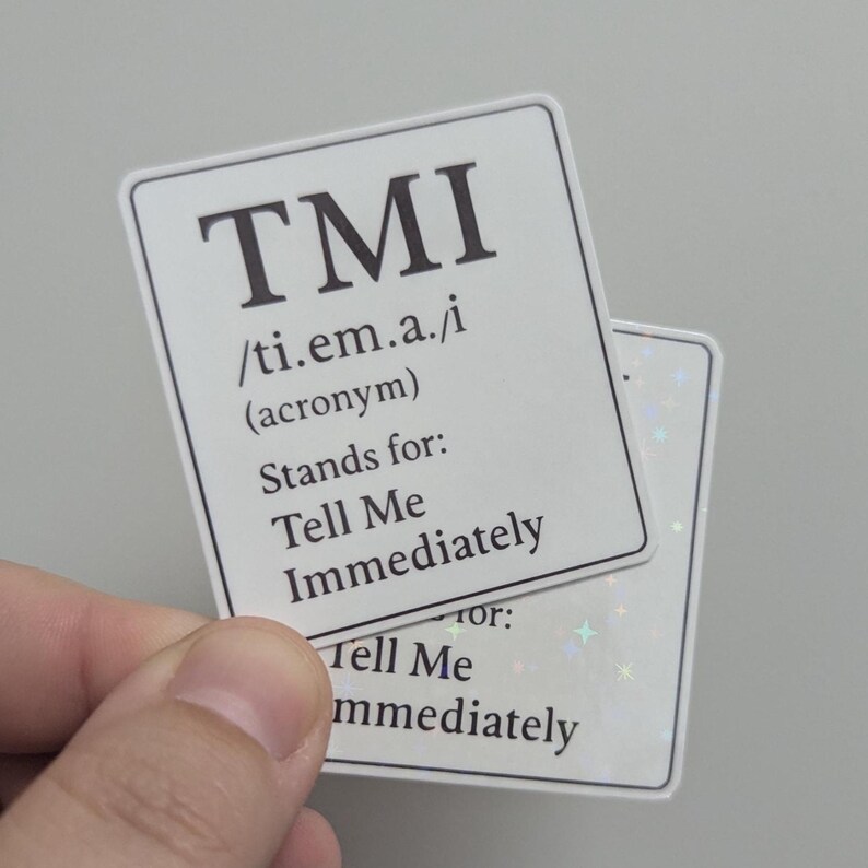 May include: Two white rectangular stickers with the acronym "TMI" in bold black letters. The stickers define "TMI" as "Tell Me Immediately". One sticker has a holographic background.