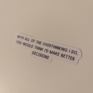 May include: A white sticker with the text: "WITH ALL OF THE OVERTHINKING I DO, YOU WOULD THINK I'D MAKE BETTER DECISIONS" in black, sans-serif font. The sticker has a rounded, cloud-like shape.