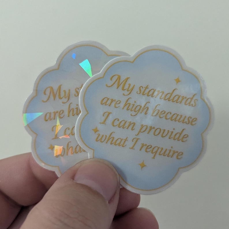 May include: Two cloud-shaped stickers with a light blue border and gold text that reads "My standards are high because I can provide what I require." The stickers have a holographic sheen.