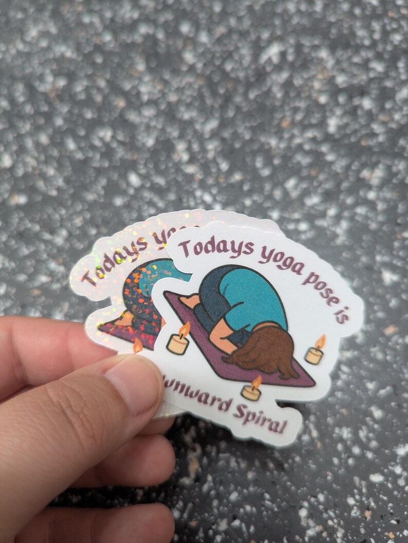 May include: Holographic stickers with the text "Todays yoga pose is downward spiral". The stickers depict a yoga pose illustration, candles, and a yoga mat.