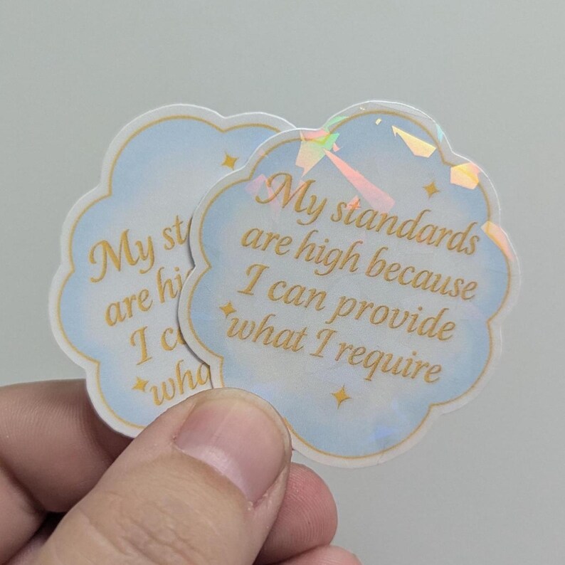 May include: Two cloud-shaped stickers with the text "My standards are high because I can provide what I require" in gold script. The stickers have a light blue background with holographic accents and small star details.