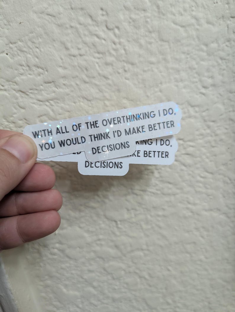 May include: Two white stickers with holographic glitter accents. The top sticker reads "WITH ALL OF THE OVERTHINKING I DO, YOU WOULD THINK I'D MAKE BETTER DECISIONS." The bottom sticker reads "DECISIONS." The stickers are held by a hand.
