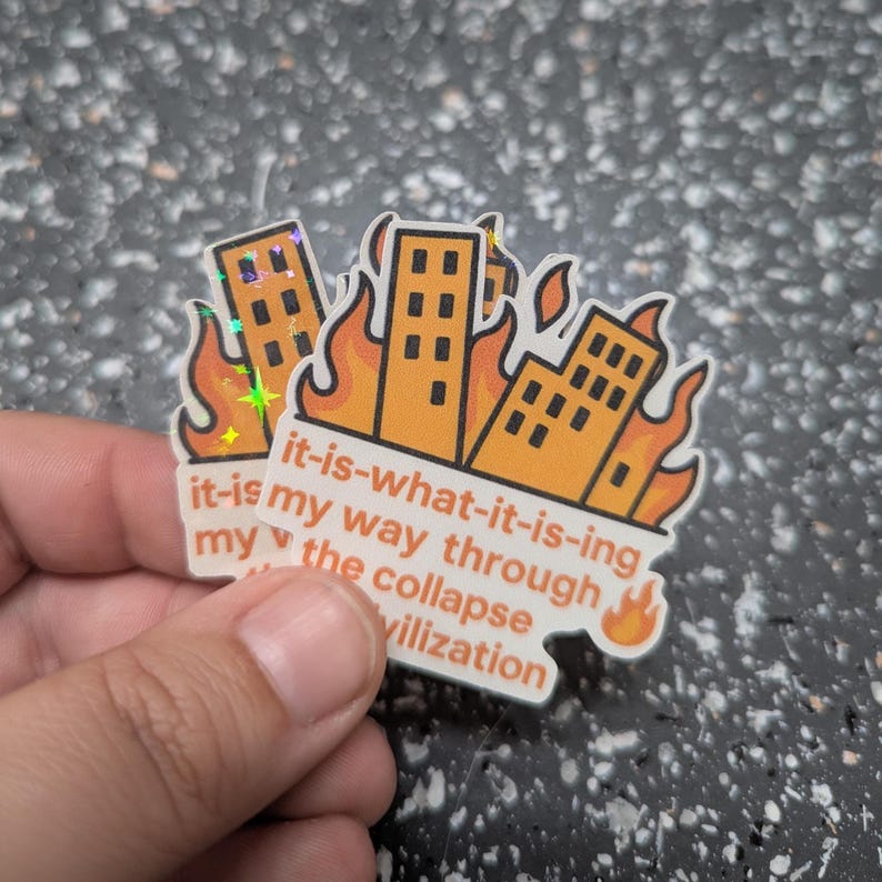 May include: A sticker featuring three orange buildings engulfed in flames. The sticker has the text "it-is-what-it-is-ing, it-is my way through my the collapse vilization". The sticker has a holographic effect.