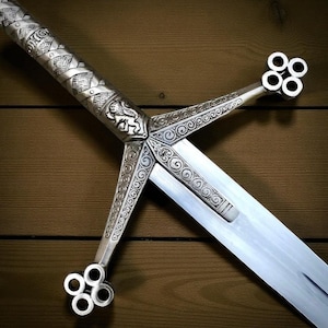 May include: A silver sword with detailed engravings. The hilt features a lion emblem and decorative patterns. The crossguard and pommel have a unique four-circle design. The blade is long and polished, reflecting light.