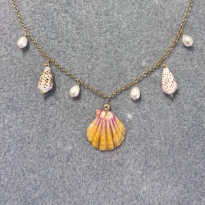 Peut inclure: Un collier doré orné d'un grand pendentif en coquillage jaune et rose, agrémenté de petites perles blanches et de deux coquillages coniques tachetés de brun. Un bijou délicat.