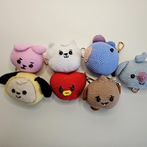 Könnte beinhalten: Eine Sammlung handgefertigter Häkel-Schlüsselanhänger in verschiedenen Formen und Farben. Die Schlüsselanhänger umfassen einen rosa Hasen, eine weiße Katze, einen blauen Ball, einen hellblauen Hund, einen gelben Hund, ein rotes Herz und einen braunen Ball. Jeder Schlüsselanhänger hat einen Metallverschluss.