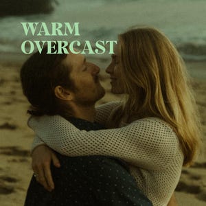 Pode incluir: Um casal se abraça em uma praia, a mulher vestindo um suéter de crochê branco e o homem vestindo uma camisa azul estampada. O texto "WARM OVERCAST" está sobreposto à imagem.