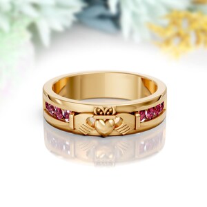 Könnte beinhalten: Ein goldener Ring mit einem keltischen Knotendesign, das ein Herz und zwei Hände zeigt. Der Ring ist mit einer Reihe von rosafarbenen Edelsteinen verziert.
