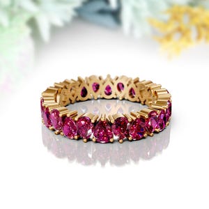 Könnte beinhalten: Ein Goldring mit einer Reihe von rosafarbenen birnenförmigen Edelsteinen.