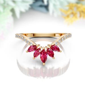 May include: A gold ring with a V-shaped band adorned with small diamonds. Five marquise-shaped red gemstones are set in the center of the ring, creating a delicate and elegant design.