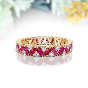 May include: A gold ring with alternating ruby and diamond gemstones. The ring features a continuous pattern of oval rubies and round diamonds set in a yellow gold band. The gemstones are set closely together, creating a sparkling effect.