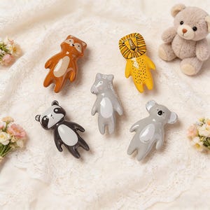 Può includere: Una collezione di figurine di animali in ceramica, tra cui una volpe, un leone, un procione, un cavallo e un koala. Le figurine sono dipinte in vari colori, come marrone, giallo, nero, grigio e bianco. È presente anche un piccolo orsacchiotto.
