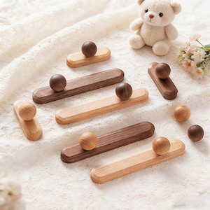 May include: Wooden decorative objects in various shades of brown and tan. Each piece features a rounded wooden ball atop a rectangular base. The objects are arranged on a white, textured surface, with a teddy bear and flowers in the background.