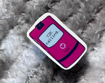 May include: A sticker featuring a pink flip phone design with the text "Y2K calling..." on the screen. The phone has a heart symbol and a camera. The sticker is on a fluffy, gray background.