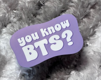May include: A lavender sticker with the text "you know BTS?" in white, bold font. The sticker has a rounded rectangular shape and is set against a fluffy, gray background.