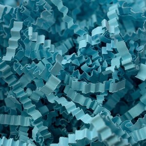 Pode incluir: Close-up de papel crepom azul claro, um material de embalagem decorativo. O papel é desfiado em tiras finas e onduladas, criando um efeito texturizado e em camadas. A cor é um azul suave e discreto, ideal para presentes.