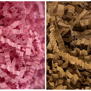Può includere: Primo piano di due sezioni di carta sminuzzata. Una sezione è rosa vibrante, l'altra è marrone caldo. La carta è tagliata in lunghe strisce ondulate, creando un riempitivo decorativo strutturato.