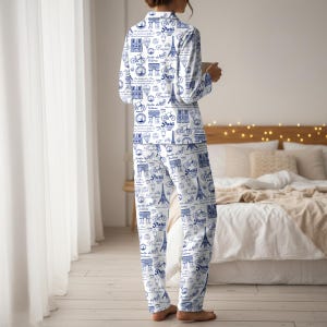 以下が含まれることがあります： 白地に青色のパリをテーマにしたプリントのパジャマセット。自転車、エッフェル塔、その他のパリのランドマークがデザインされています。長袖トップスとパンツは柔らかい生地で作られています。
