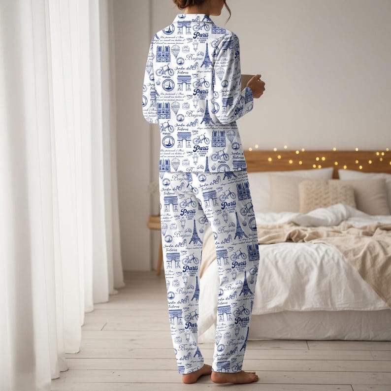 以下が含まれることがあります： 白地に青色のパリをテーマにしたプリントのパジャマセット。自転車、エッフェル塔、その他のパリのランドマークがデザインされています。長袖トップスとパンツは柔らかい生地で作られています。