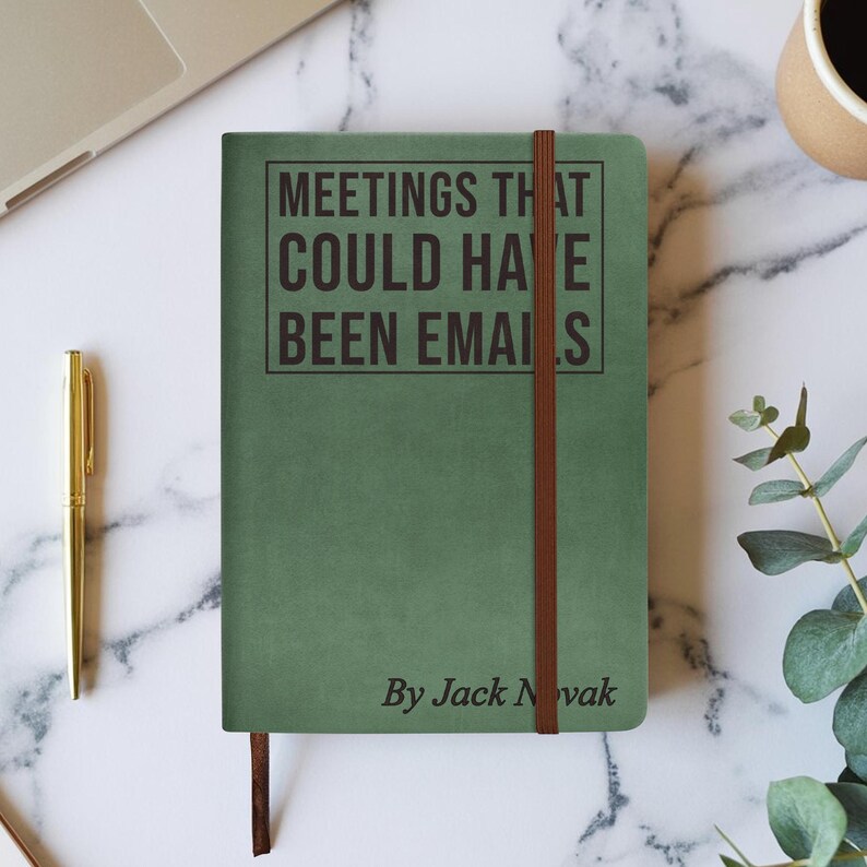 Op de afbeelding: Een groen notitieboek met de tekst "MEETINGS THAT COULD HAVE BEEN EMAILS" in het zwart. Het notitieboek heeft een bruine elastische band en de naam van de auteur, "By Jack Novak", onderaan. Een gouden pen en een laptop zijn zichtbaar op de achtergrond.
