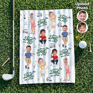 May include: A golf towel with a blue and white striped pattern featuring cartoon illustrations of children playing golf. The towel has the text "Best Dad By Par" in green and white. Golf clubs, balls, and tees are also visible.