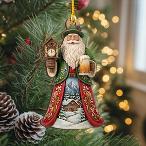 May include: A Christmas ornament depicting Santa Claus in a green coat and red robe, holding a cuckoo clock and a beer stein. The robe features a winter landscape scene. The ornament is hanging from a gold string.