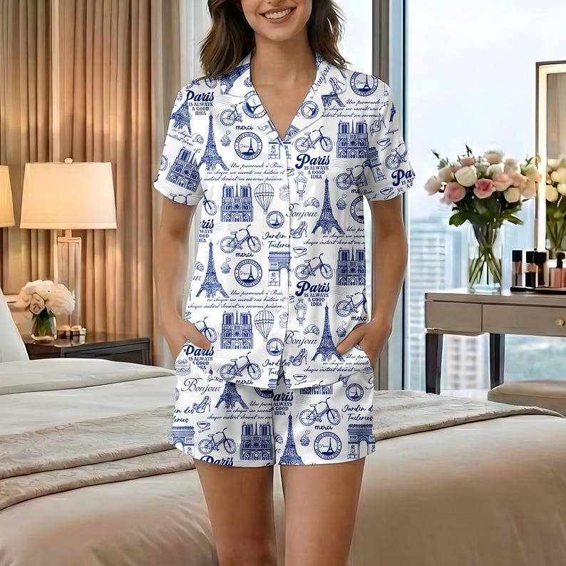以下が含まれることがあります： パリをテーマにした青いプリントの白いパジャマセット。半袖のボタンダウンシャツとマッチするショーツが含まれています。プリントには、エッフェル塔、自転車、そして「Paris is always a good idea」というテキストが描かれています。