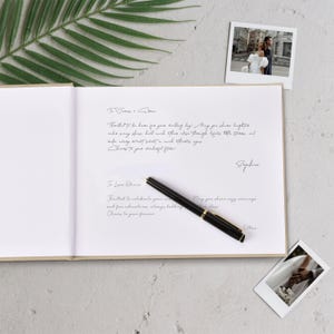 May include: An open wedding guest book with handwritten messages and a black pen with gold accents. Two polaroid photos of a wedding couple are also visible, along with a green leaf.