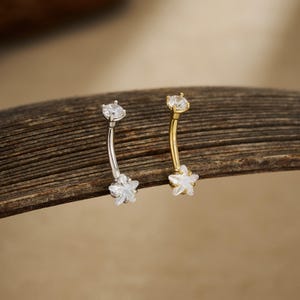 Puede incluir: Dos piercings para el ombligo. Uno es de color plateado, el otro dorado. Ambos tienen un diseño de barra curva. Cada anillo presenta una gema transparente y redonda en la parte superior y una gema en forma de estrella en la parte inferior.