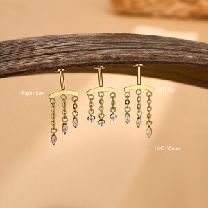 Op de afbeelding: Drie goudkleurige oorbellen met platte achterkant, gebogen staven en drie bungelende kettinkjes, elk eindigend in een heldere steen in marquise-slijpvorm. De tekst Right Ear, Left Ear en 16G/6mm is zichtbaar op de afbeelding.
