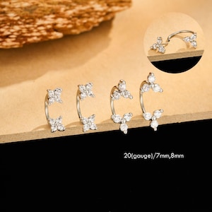 May include: Silver-toned, curved earrings with clear, sparkling gemstones arranged in floral and cluster designs. The earrings are displayed on a light brown surface. Text on the image reads: 20(gauge)/7mm,8mm.