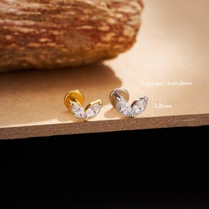 May include: Two leaf-shaped stud earrings. One is gold-toned, the other is silver-toned. Each earring features two clear, sparkling stones. The text on the image reads "16(gauge)/6mm,8mm" and "3.8mm".