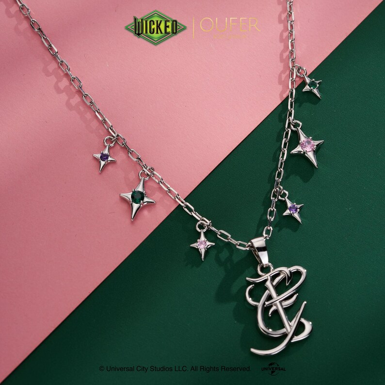 May include: Silver necklace with a pendant of stylized initials and star charms. The stars have purple, green, and pink gemstones. The background is split diagonally, with pink and green sections.