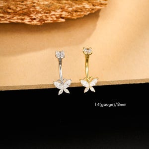 May include: Two belly button rings, one silver and one gold, each with a butterfly design. The butterfly has clear, sparkling accents. The text "14(gauge)/8mm" is visible.