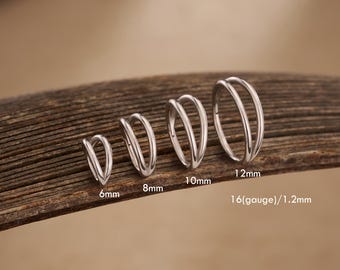 May include: A set of silver-colored double hoop earrings in various sizes: 6mm, 8mm, 10mm, and 12mm. The earrings are displayed on a wooden surface, with the size of each earring clearly labeled in millimeters and the gauge size.