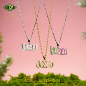 Op de afbeelding: Drie kettingen met "WICKED" hangers. Eén heeft een zilveren ketting en een hanger met heldere stenen, een andere een gouden ketting en een hanger met heldere stenen, en de derde een zilveren ketting met een groene en roze stenen hanger.