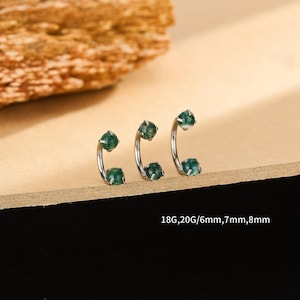 Puede incluir: Tres pendientes de barra curvados de color plateado con detalles de piedras preciosas verdes. Los pendientes se muestran sobre una superficie marrón claro. El texto de la imagen dice: 18G,20G/6mm,7mm,8mm.