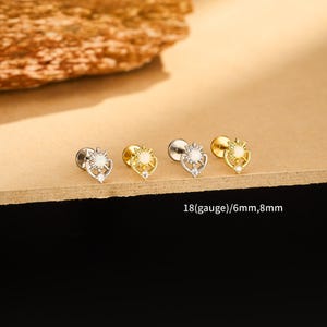 May include: A collection of four small, decorative earrings. Two are silver-toned, and two are gold-toned. Each earring features a sunburst design with a central white stone and a small, clear gem. Text on the image reads: 18(gauge)/6mm,8mm.