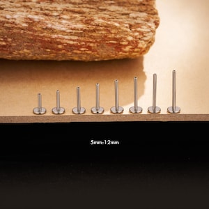 May include: A collection of silver-colored lip piercing studs, ranging in size. The studs are arranged in a row, with the smallest on the left and increasing in size to the right. The text "5mm-12mm" is visible.