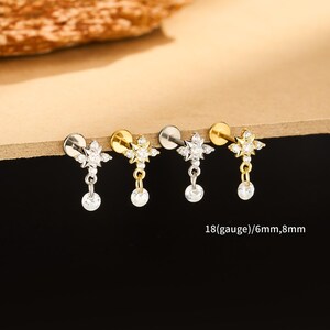 May include: Four ear piercing studs. Each stud features a starburst design with clear crystals and a dangling round crystal. The studs are available in silver and gold tones. Text on the image reads: 18(gauge)/6mm,8mm.