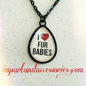 May include: A black chain necklace with a teardrop-shaped pendant. The pendant has a white background with the text "I love fur babies" and a red heart.