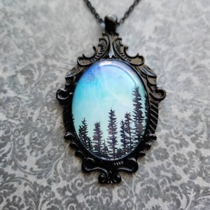 May include: A black metal pendant necklace with a glass cameo featuring a watercolor painting of a forest silhouette against a blue and white sky.