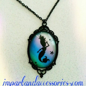 May include: Black necklace with a cameo pendant featuring a silhouette of a mermaid with a star in a blue, green, and pink ombre background.