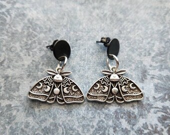 May include: A pair of silver earrings featuring a moth design with crescent moons and stars. The earrings have black rubber backs.