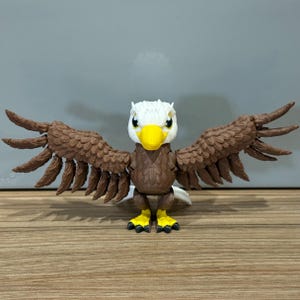 May include: A brown and white eagle figurine with outstretched wings. The eagle has a yellow beak and yellow feet.