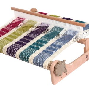 May include: A wooden loom with a colorful woven fabric on it. The loom has two wooden spools on the ends and a wooden bar across the top.