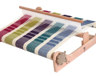 May include: A wooden loom with a colorful woven fabric on it. The loom has two wooden spools on the ends and a wooden bar across the top.