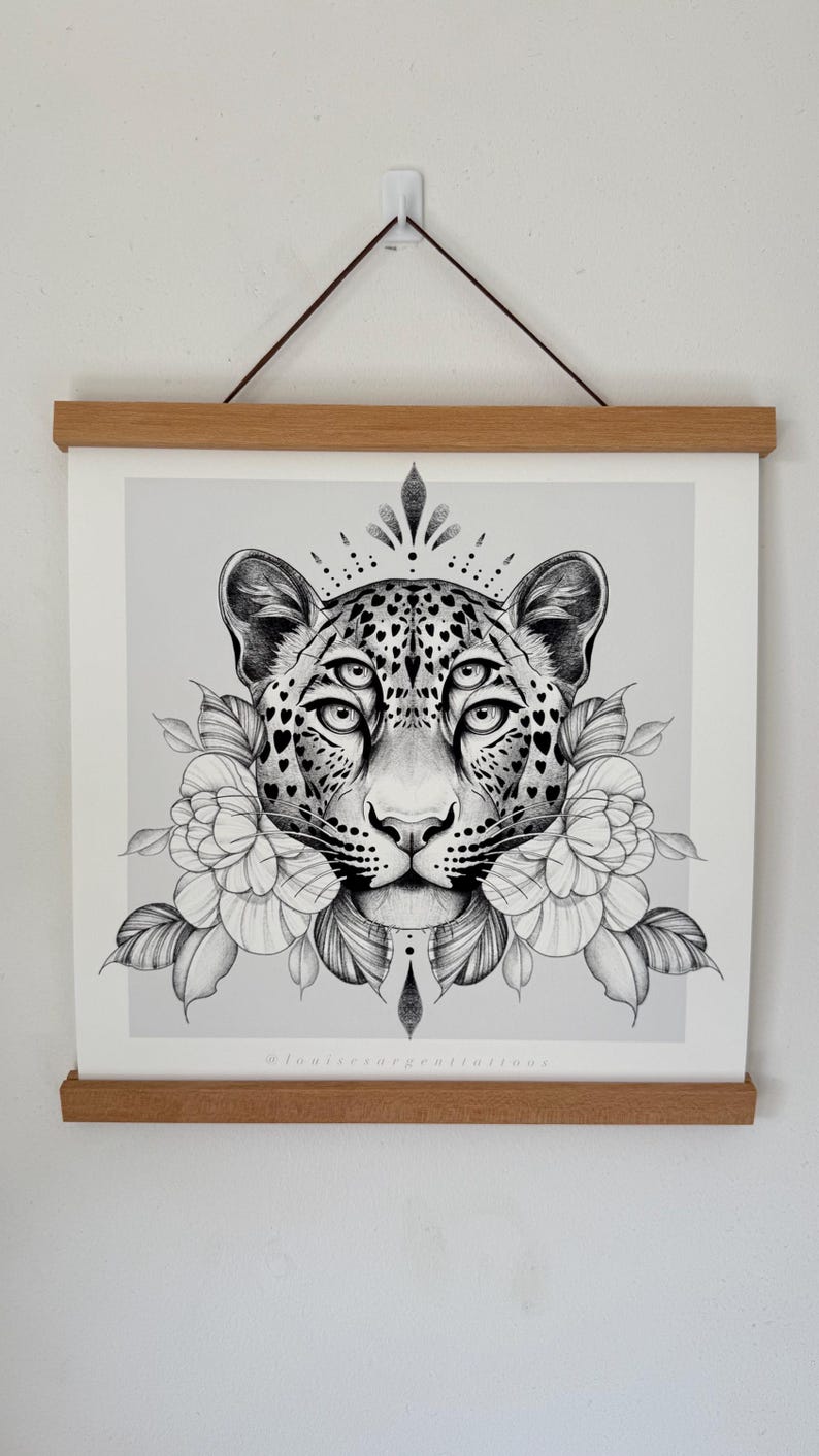 May include: Black and white illustration of a leopard with multiple eyes, adorned with floral elements and a crown-like design. The artwork is displayed on a light gray background and framed with wooden bars.